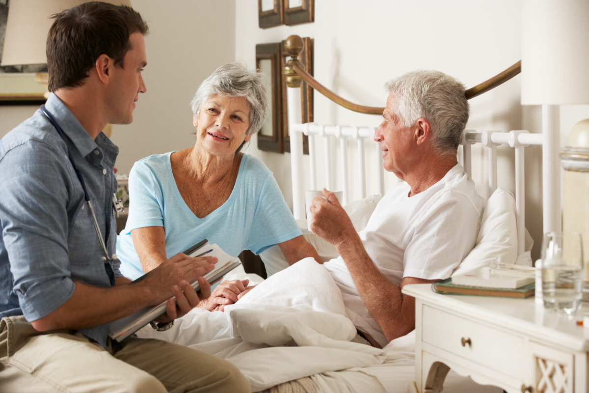 Hospice clinician sitting at the bedside talking with a patient and his wife