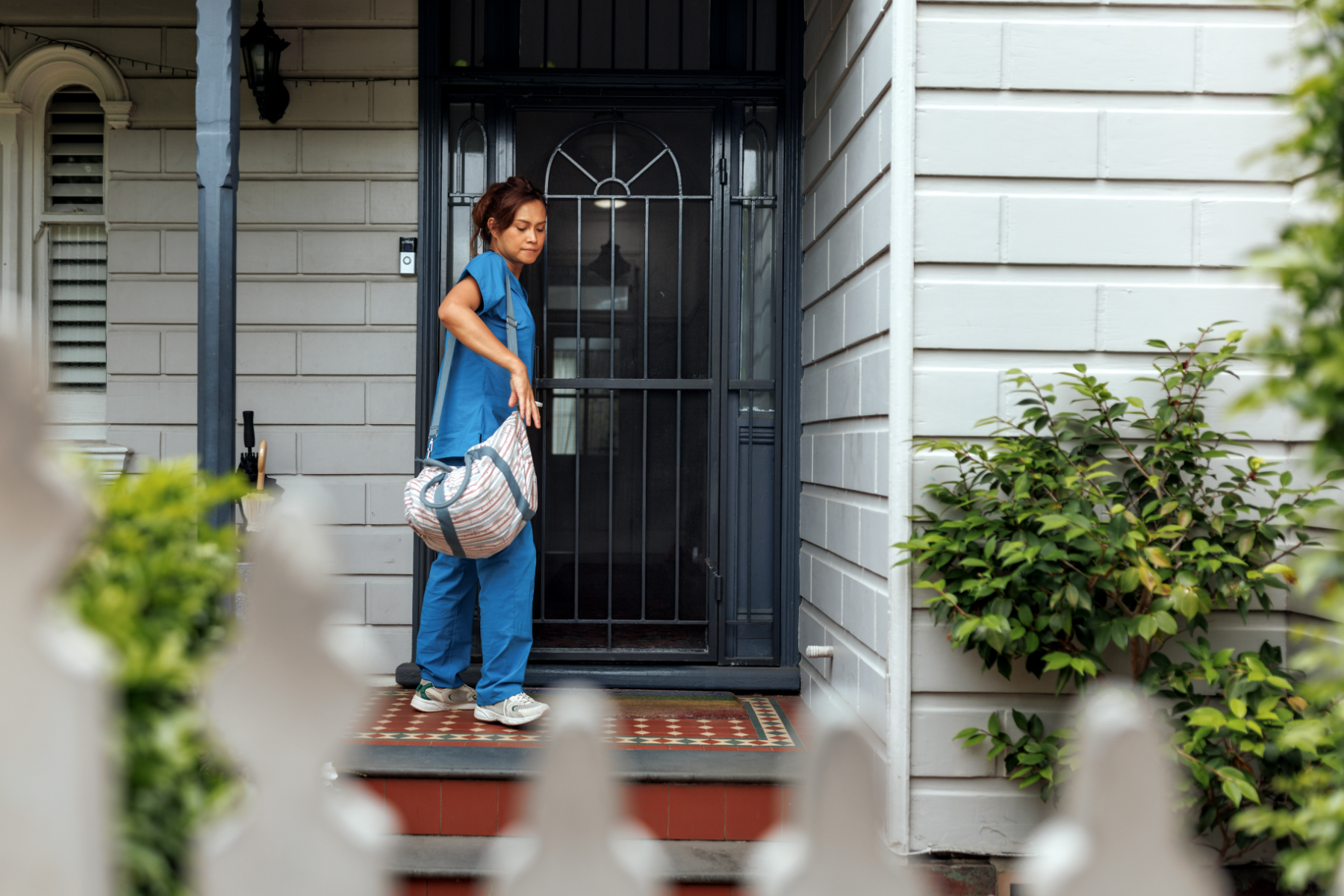 Home health nurse in scrubs carrying a visit bag up the steps to a client's front door