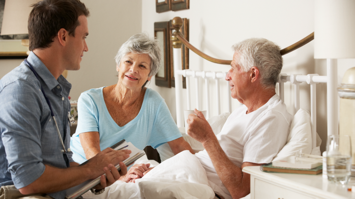 Hospice clinician sitting at the bedside talking with a patient and his wife